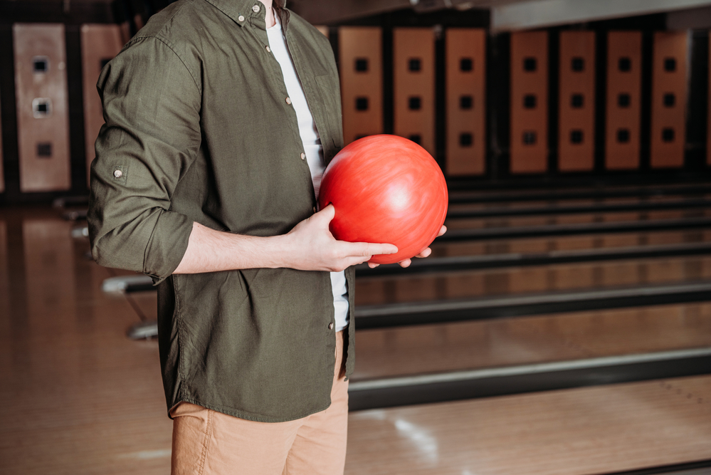 Male bowler holding red bowling ball will take one step forward to get out of the stance.